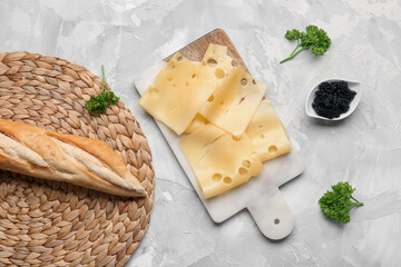 Board with tasty cheese slices, parsley, black caviar and baguette on light background