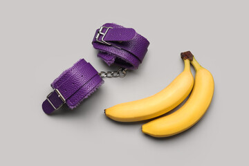 Handcuffs from sex shop and tasty bananas on grey background