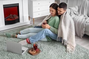 Happy couple with glasses of warm mulled wine watching movie while sitting on floor in living room