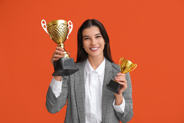 Young businesswoman with gold cups on orange background