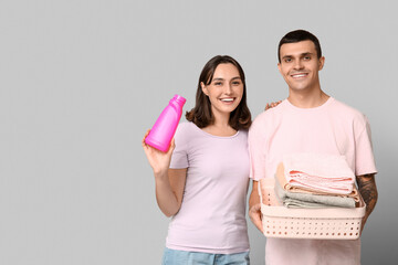 Young couple with laundry basket and bottle of detergent on grey background