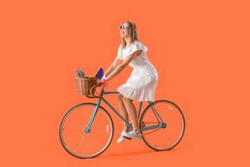 Young woman with flag of France riding bicycle on orange background