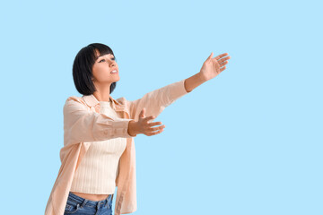 Young woman opening arms for hug on blue background