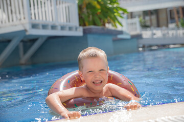 Little boy bathing in swimming pool with lifebuoy donut, smiling and happy