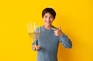 Little Israeli boy in kipa pointing at menorah on yellow background
