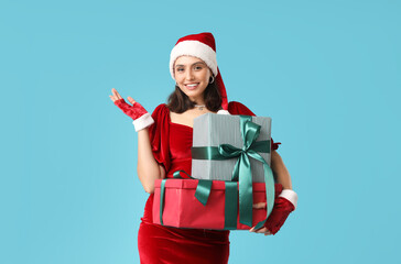 Fototapeta na wymiar Happy young woman in Santa hat with Christmas gift boxes on blue background