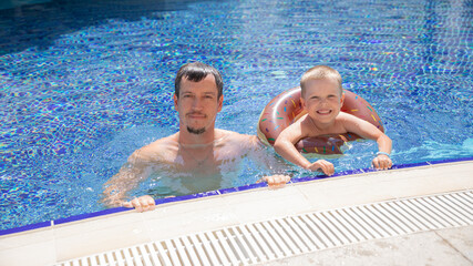 Little boy and his father bathing in swimming pool with lifebuoy donut, smiling and happy