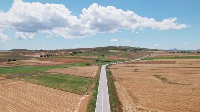 Drone dolly above empty grey asphalt road between grassland farm plots