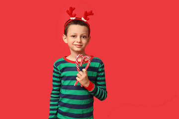 Cute little boy in pajamas with candy canes on red background