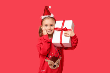 Cute little girl in Christmas sweater with gift on red background