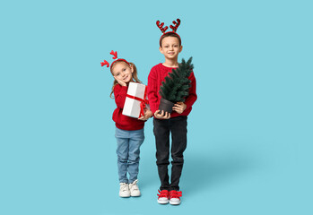 Cute little children in reindeer horns with Christmas gift and tree on blue background