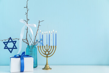 Menorah, gift box, vase with branches and David star on white table near blue wall, closeup....