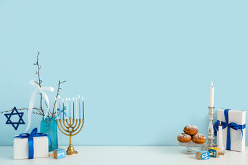 White cabinet with menorah, sufganiyots, dreidels and gift boxes near blue wall. Hanukkah celebration