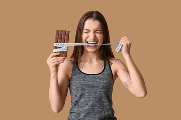 Young woman with chocolate bar and tape measure on brown background - Powered by Adobe