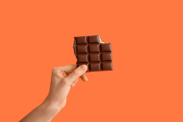 Female hand with sweet chocolate bar on orange background