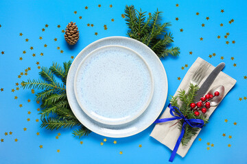 Beautiful table setting with Christmas tree branches, pine cone and confetti on blue background