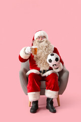 Santa Claus with mug of beer and soccer ball in armchair on pink background