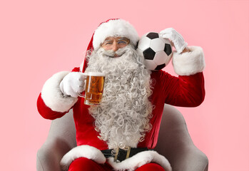 Santa Claus with mug of beer and soccer ball in armchair on pink background