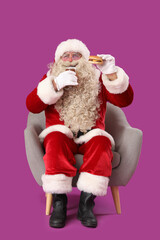 Santa Claus with glass of beer and tasty burger in armchair on purple background