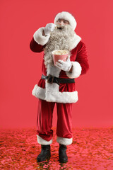 Santa Claus with tasty popcorn on red background