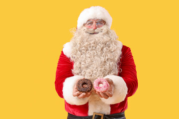 Santa Claus with tasty donuts on yellow background