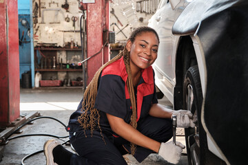 Black female automotive mechanic worker screws car wheel nuts with wrench for repair at garage, vehicle maintenance service jobs, industry occupation business, happy labor works, smile and cheerful.