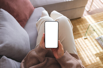 Top view mockup image of a woman holding mobile phone with blank desktop white screen while lying...