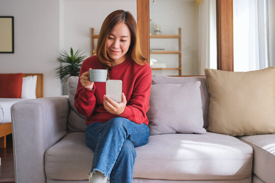 Portrait image of a beautiful young woman holding coffee cup and using smart phone at home