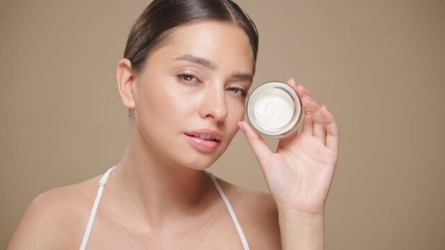 Portrait young woman uses creams of her face. Concept for fresh moisturized skin beautiful closeup cosmetic face happy healthy model.   Model with a jar of face cream
