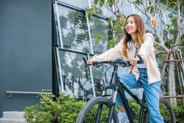 Naklejka na ściany i meble Happy Asian young woman riding bicycle on street outdoor near building city, Portrait of smiling female lifestyle use mountain bike in summer travel means of transportation, ECO friendly, Urban biking