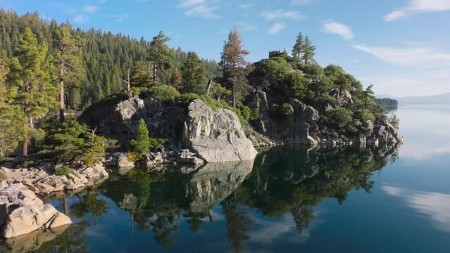 Scenic aerial of rocky island in middle of lake 4K. Natural landscape of Tahoe lake and mirror like reflection water surface with scenic clouds. Beautiful nature of Tahoe lake and emerald bay island