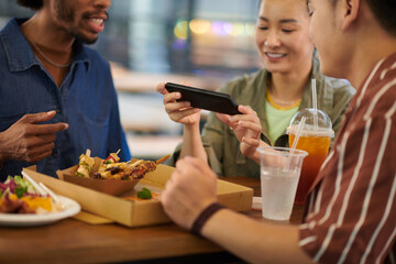 Smiling woman taking photo of meat skewers friends bought for lunch