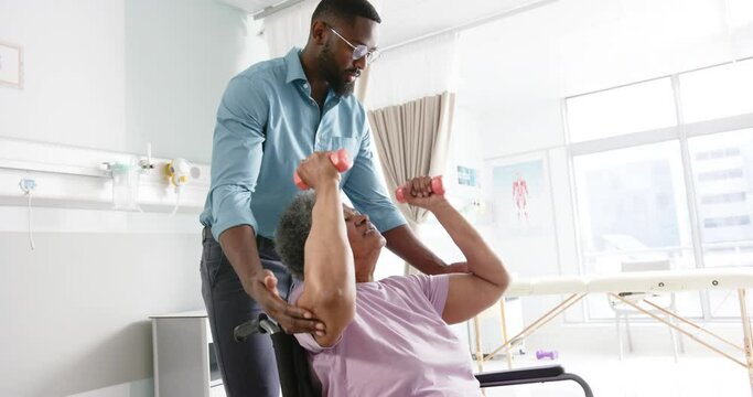 African american woman exercising with weights and male doctor advising in hospital, slow motion
