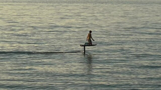 Unrecognizable man riding electric foil or electro SurfBoard on sea surface.