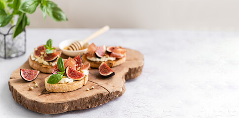Tasty bruschetta banner. Bruschetta with ciabatta baguette, Parma ham, cream cheese, figs, basil, honey and walnut on wooden board on white background. Antipasti. Copy space. Canape, sandwiches