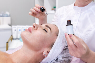 Close up of professional cosmetologist applies moisturizing serum to client woman's face. Concept...