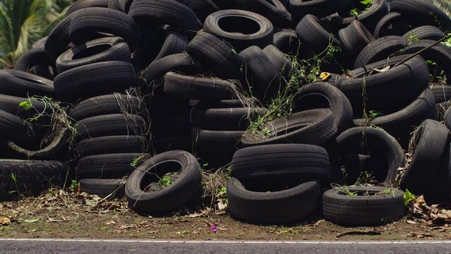 A dump of old tires and bikes and cars pass in front of them, the old generation and the new, rubber rubbish, a mountain of unnecessary old tires, tires in the grass in Bali, a lot of old rubber.