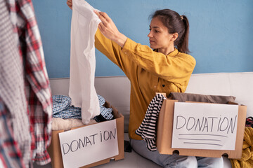 Donation, charity, volunteer concept. Woman putting Clothes into donation boxes at home for support...