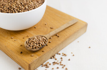 Organic dry buckwheat groats in a white bowl with a wooden spoon on a wooden cutting board. Rural style. Vegetarian and vegan food. Concept of healthy eating. Horizontal orientation. Selective focus