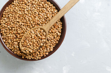 Organic dry buckwheat groats in brown bowl with wooden spoon on gray background. Vegetarian and...