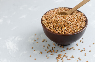 Organic dry buckwheat groats in brown bowl with wooden spoon on gray background. Vegetarian and vegan food. Concept of healthy eating. Horizontal orientation. Copy space.