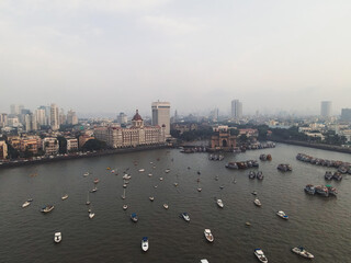 Aerial view of Gateway of India. Cityscape of old Mumbai town. Early morning weather on the seashore of Mumbai. Drone view of Taj Palace Hotel. Fishing boats sail in the sea during sunrise.