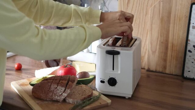 Young woman shoving slices of bread into toaster oven. Breakfast concept. 4k footage