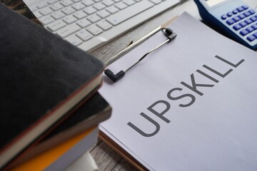 Closeup image of paper clipboard with text UPSKILL on office office desk.