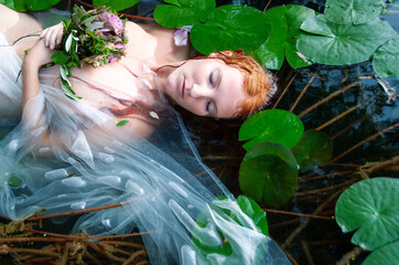 Gorgeous beautiful portrait of young sexy woman Ophelia with red hair lying peaceful, quiet, calm...