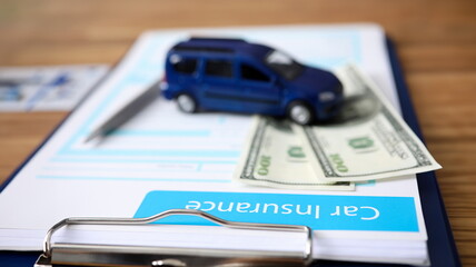 Close-up of important documents about car insurance. Blue toy machine and pencil lying on currency banknotes and paper folder on table. Assurance concept