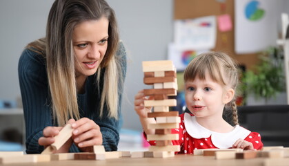 Portrait of little girl enjoying spending time with lovely mum. Thoughtful child with angel face playing with building kit. Childhood and parenthood concept