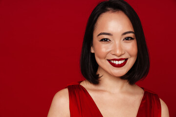 Beautiful asian woman smiling at camera while standing isolated over red background