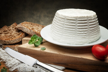 Ricotta cheese with bread, tomatoes and fresh oregano on cutting board, space for text.