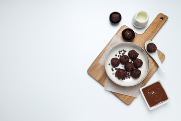 Brigadeiro on kitchen board and bowl with chocolate on white background, space for text